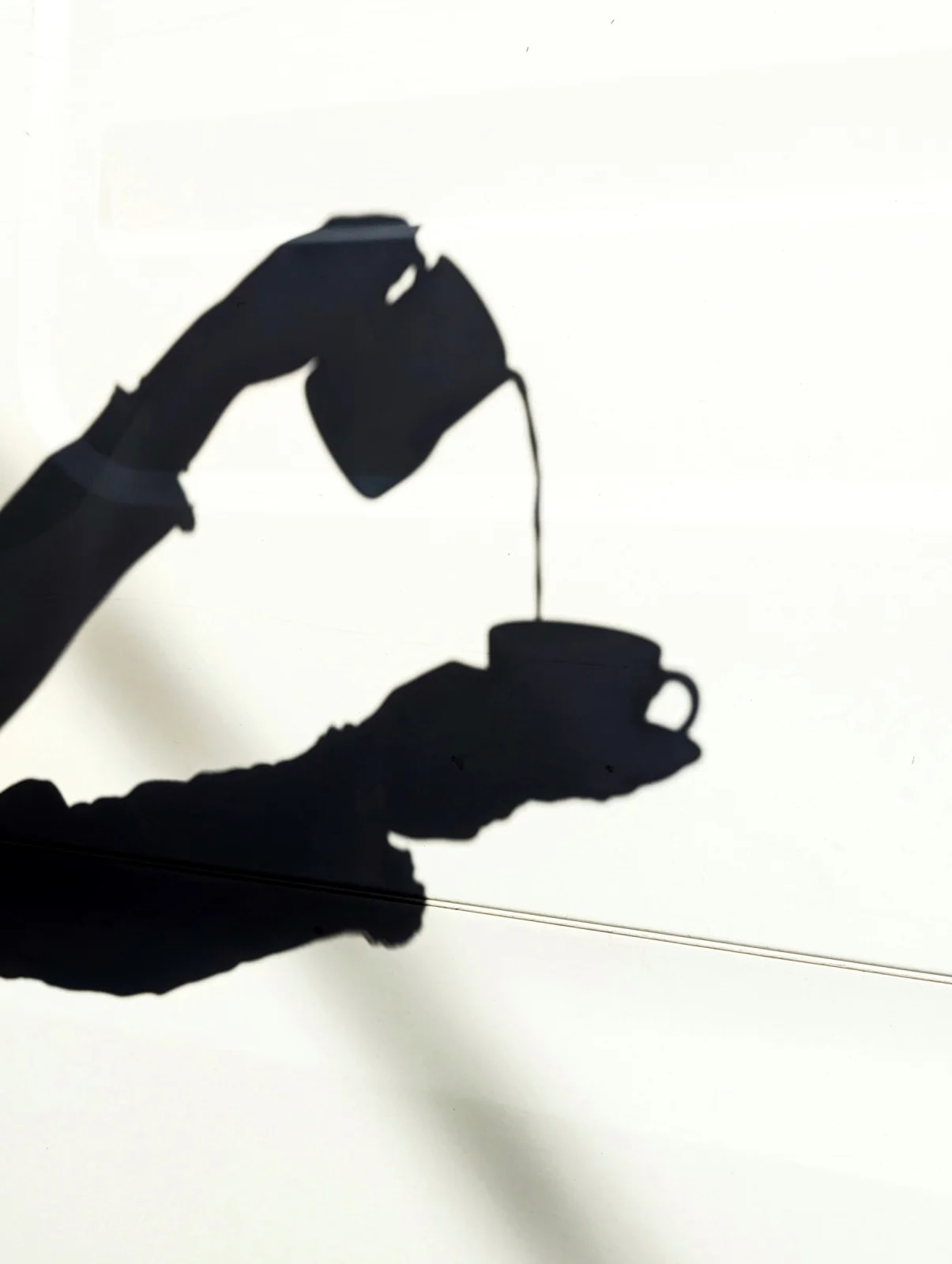 Silhouette of a hand pouring coffee into a cup